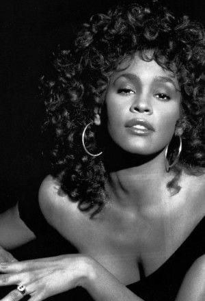 a black and white portrait of a woman with curly hair and large hoop earrings, posing against a dark background.