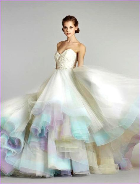 a beautiful bride stands in a white wedding dress with a rainbow of pastel colors layered underneath the skirt. she is looking at the camera with a soft smile on her face. the dress is strapless and has a sweetheart neckline. the bride's hair is styled in a simple updo. she is wearing a delicate necklace and earrings. the dress is billowing out around her, and the colors of the tulle skirt are vibrant and cheerful. the overall feel of the image is romantic and dreamy.