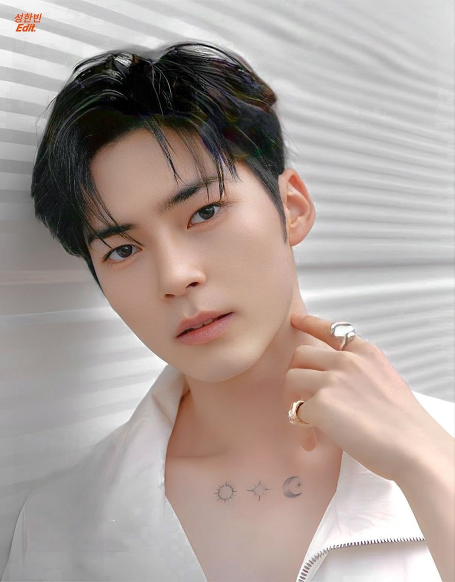 a closeup portrait of a young asian man with dark hair and a white shirt. he's posing against a white textured background and looking directly at the camera. he has a sun and moon tattoo on his chest.
