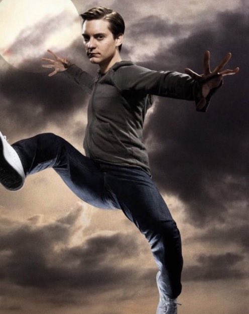 actor andrew garfield as spiderman in a dynamic jump against a dramatic night sky. he wears a dark gray hoodie and jeans, and his pose suggests agility and power. the lighting emphasizes his silhouette and creates a sense of action. the overall mood is dramatic and heroic.
