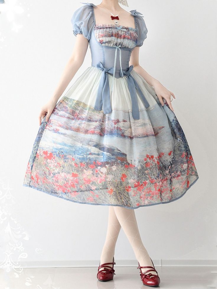 a woman is standing wearing a romantic, floral print dress. the dress is white with a blue, pink, and red floral print. it has puff sleeves and a midi length. the woman is also wearing red mary jane shoes. the background is white.