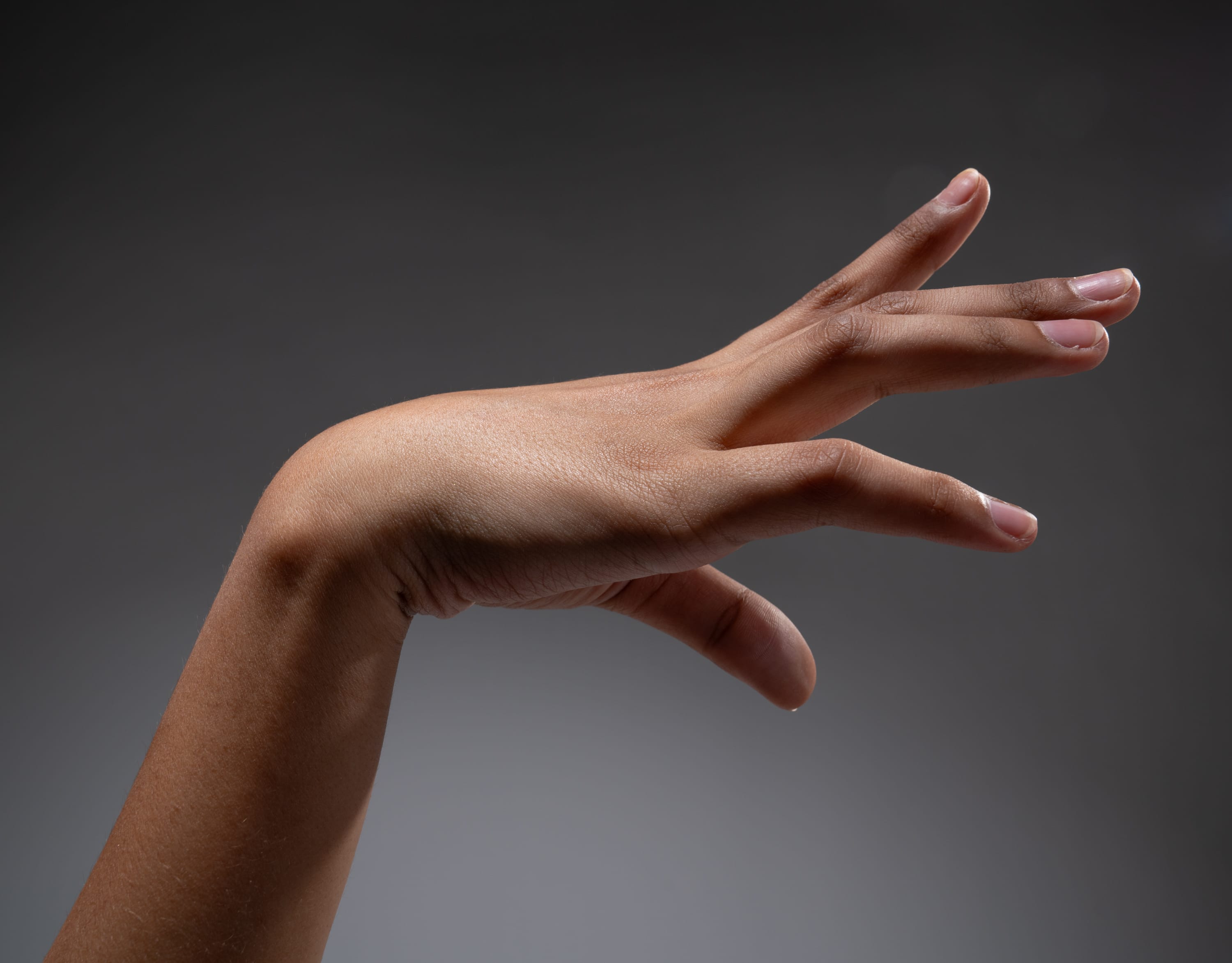 a black woman's arm and hand are outstretched against a gray background. the hand is open, with the fingers slightly spread. the image is lit from above, creating a soft shadow below the hand.
