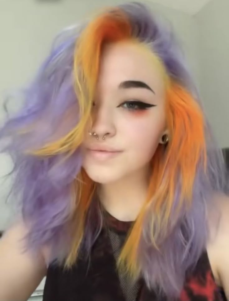 a portrait of a woman with colorful hair. her hair is styled with a mix of purple, orange, and yellow. she has multiple piercings in her nose and ears. she is wearing eyeliner and smiling slightly. the background is a neutral, light color.