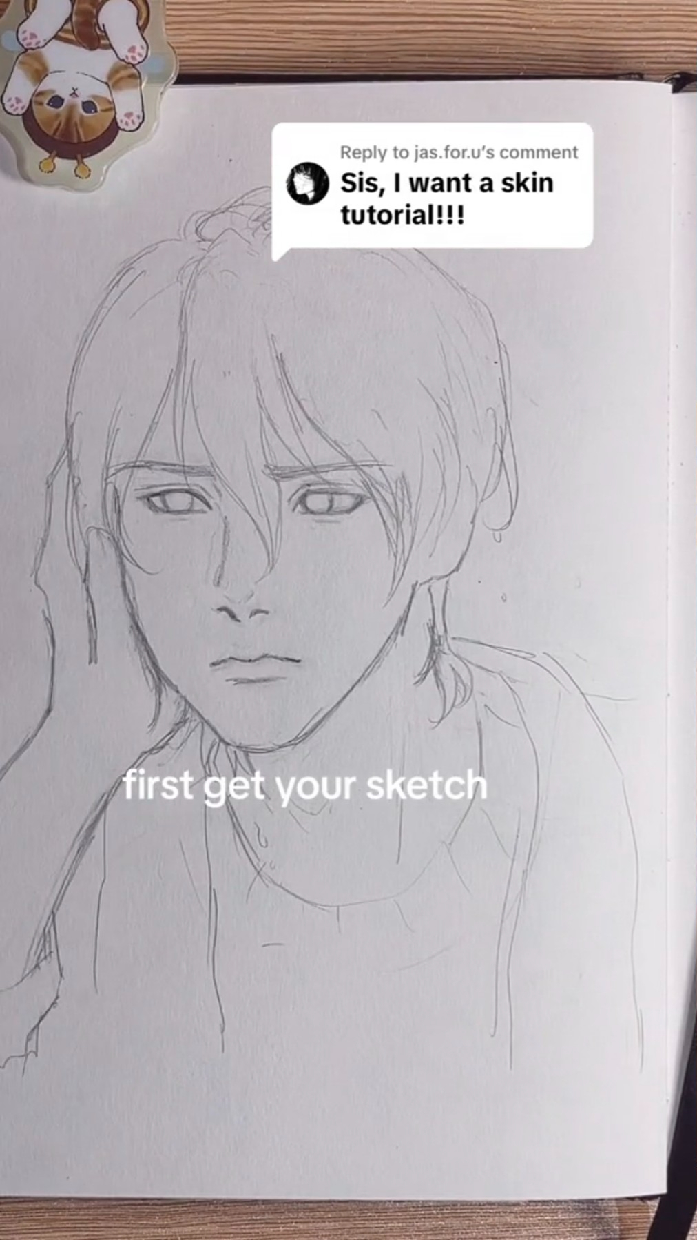 a handdrawn sketch of an animestyle male character is shown on a sketchbook page. the drawing is in its early stages, focusing on basic facial features and hair. a text bubble at the top of the image contains a comment requesting a skin tutorial. below the character's face, a caption reads "first get your sketch," indicating the initial step of the tutorial. a small, decorative magnet featuring a cat illustration is visible at the top left corner of the sketchbook.