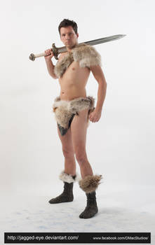 the image shows a muscular male model posing as a barbarian or warrior. he is wearing a fur shoulder piece and loincloth,  fur boots, and is holding a large sword across his shoulders. the backdrop is plain white, highlighting the model and his attire. the pose suggests strength and readiness for battle.  the overall style evokes a fantasy or historical setting.