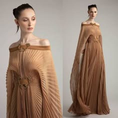 two women are wearing identical pleated, long sleeve, floorlength gowns. the gowns have a cape like overlay and both women are wearing gold jewelry. the women are standing facing the camera.