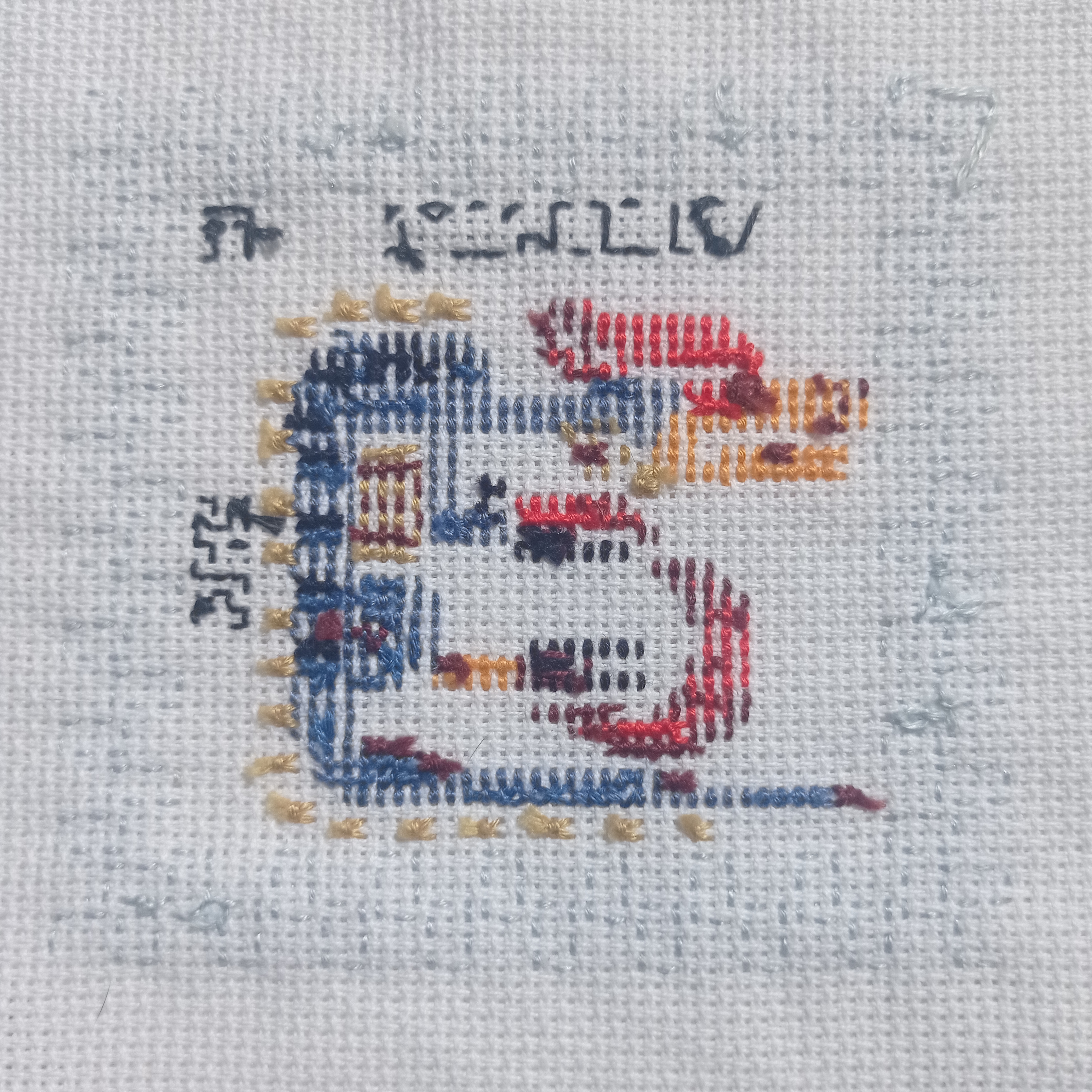 this is a closeup image of an unfinished crossstitch project.  the project is of a small, stylized, colorful dragon. the dragon has been partially stitched onto a piece of white aida cloth. you can see the pattern, printed in grey, on the aida cloth around the partially completed stitching.