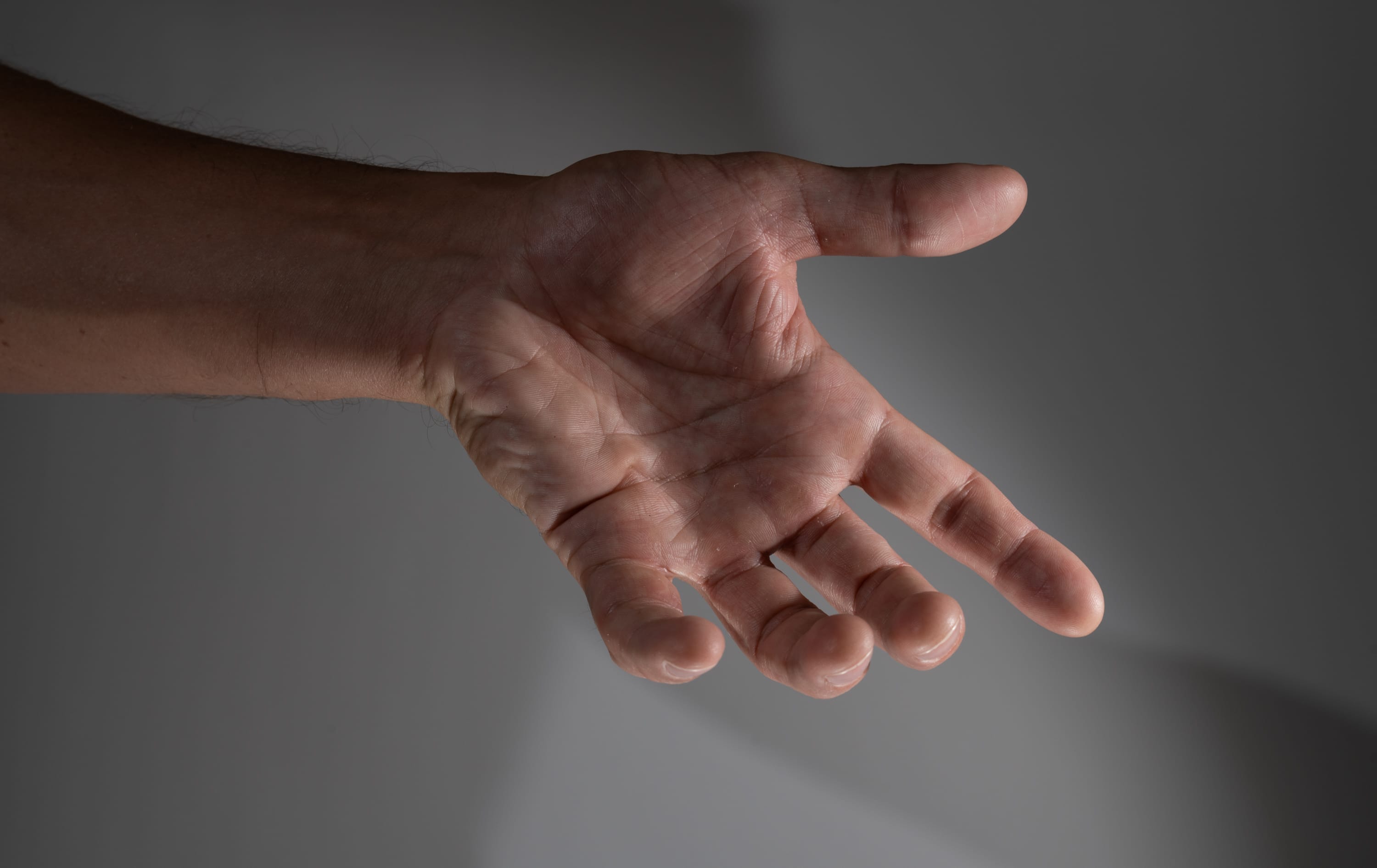 the image shows a closeup of a man's outstretched right hand. the hand is slightly cupped, as if reaching out for something. the lighting is soft and natural, highlighting the texture of the skin and the wrinkles on the palm. the overall color palette is muted and earthy, with shades of beige, brown, and gray.