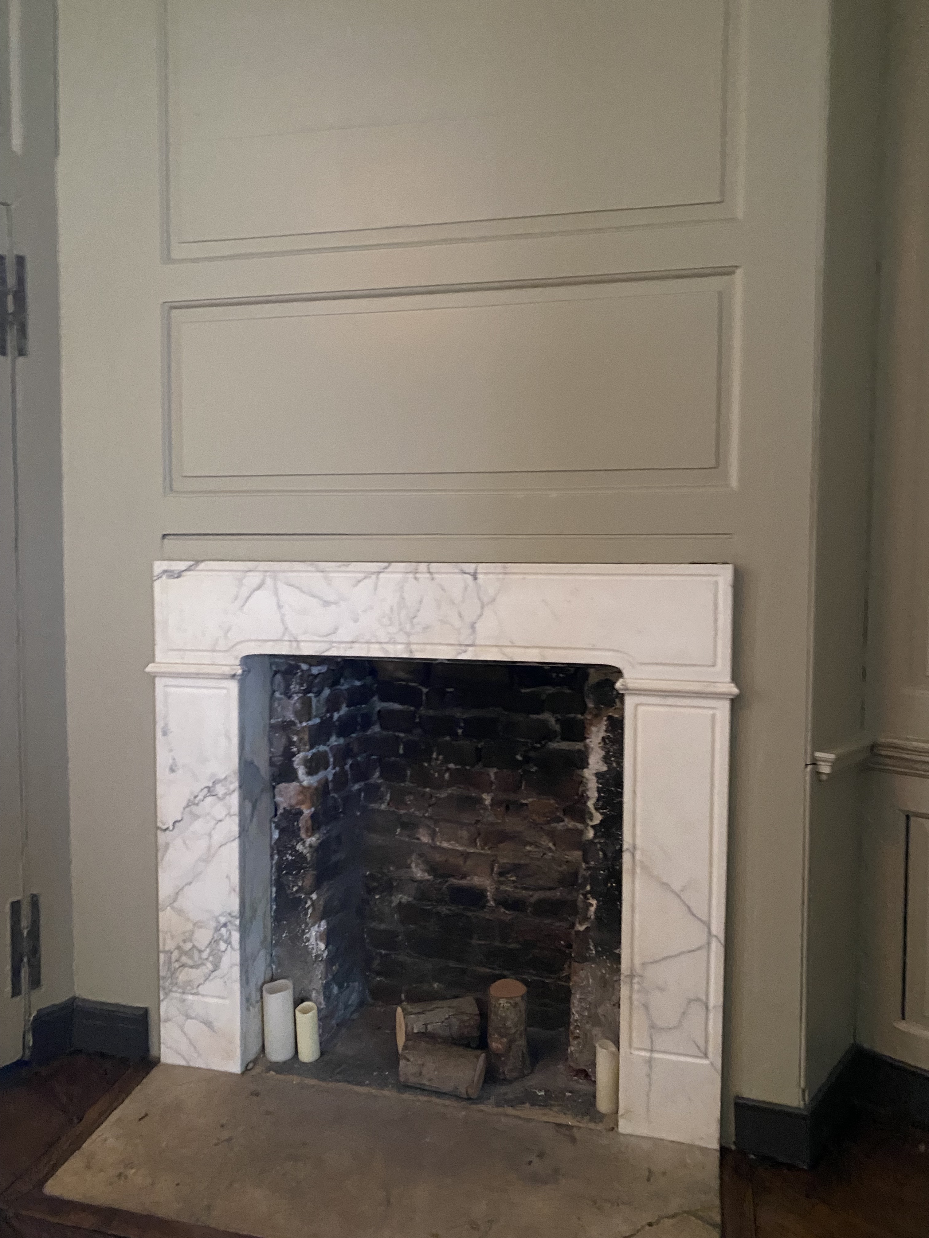 a fireplace with a marble mantle, surrounded by paneling, featuring a brick interior, logs, candles, and a hearth.