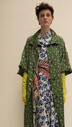 a fashion model is shown in a studio portrait, with a green coat with a floral print, and a floral print dress underneath. the model is looking at the camera.