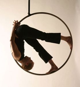 a silhouette of a woman performing an aerial hoop routine. she is upside down, with her feet in the air and her body contorted around the hoop. the hoop is positioned in a circular shape, creating a dramatic visual. the woman's silhouette is elegant and graceful, showcasing her strength and flexibility. the image captures the beauty and athleticism of aerial hoop performance.