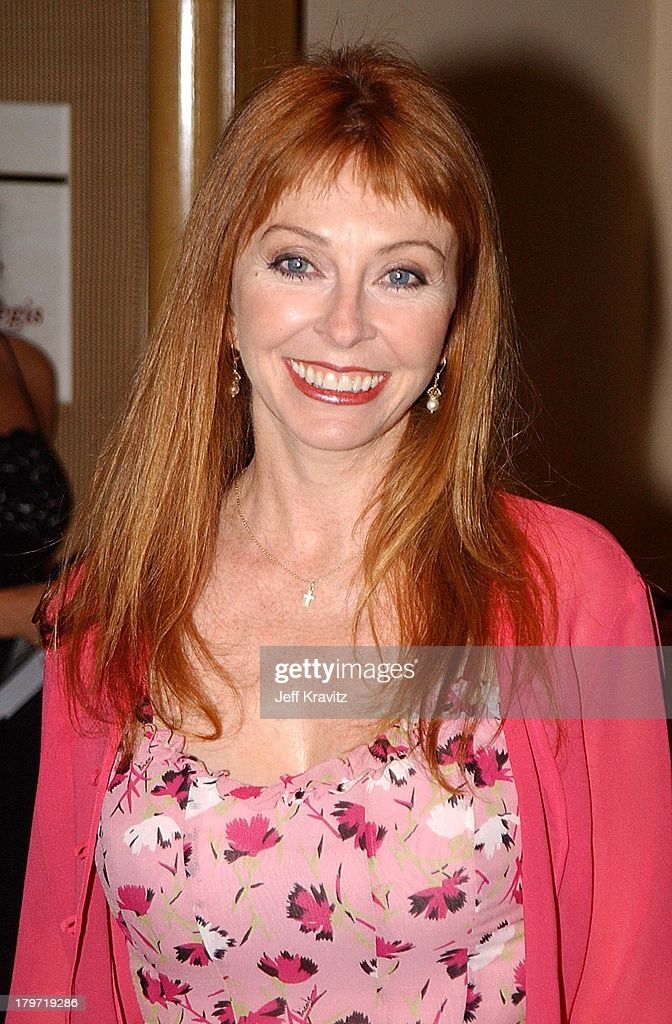 a woman with long red hair is smiling. she is wearing a pink shirt and looking at the camera.  the background is light, giving the photo a studio look.