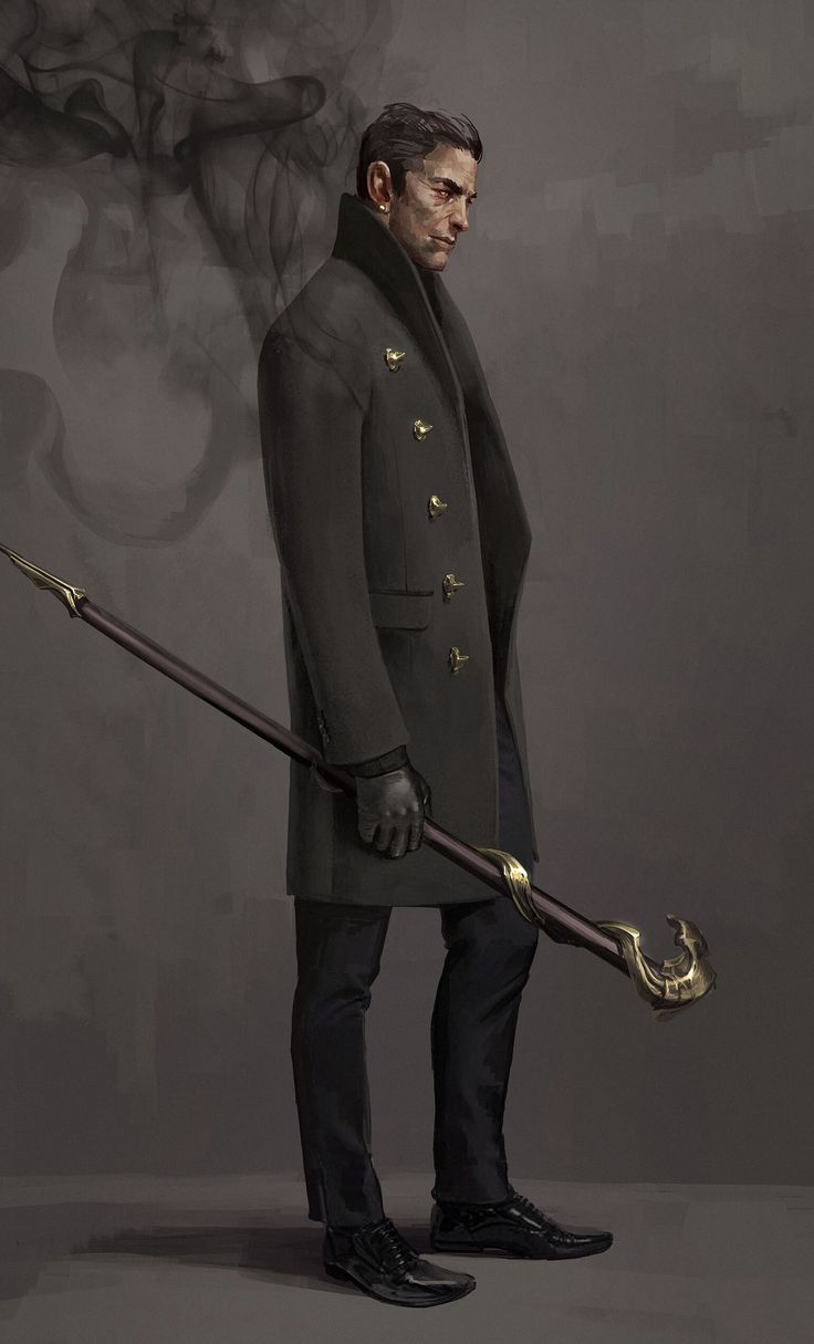 a man in a dark suit and coat is standing holding a decorative goldtipped staff, and looking at the ground, his expression serious. the man is posed in a studio setting against a gray background with smoke behind him.