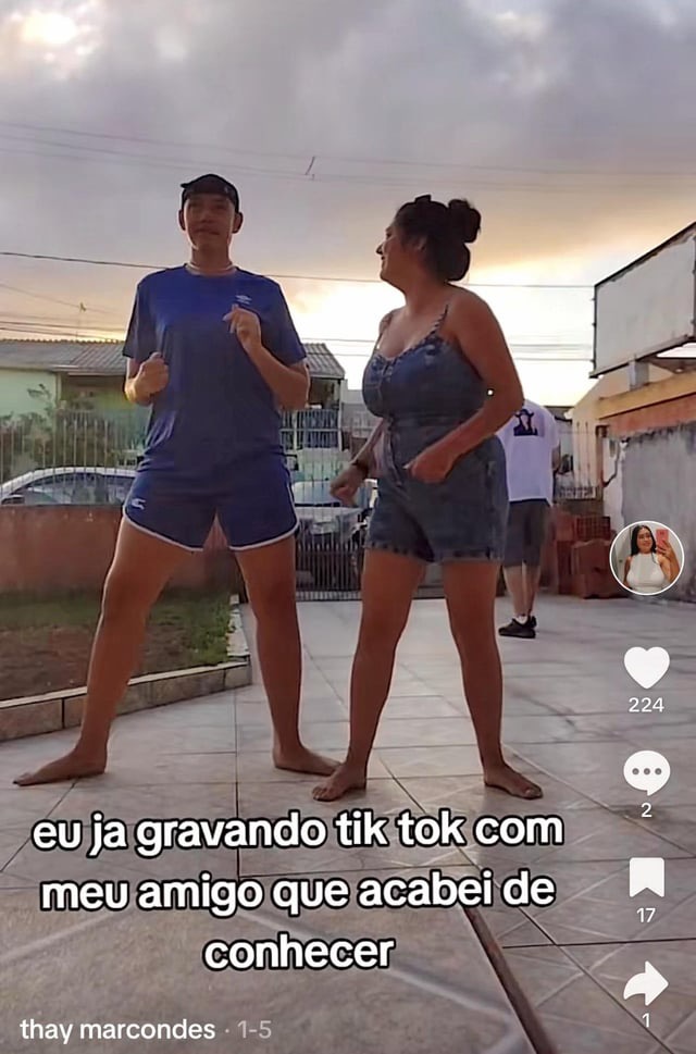 a young man and woman are standing on a sidewalk, dancing and recording a tik tok video. the man is wearing blue shorts and a tshirt, while the woman is wearing denim shorts and a tank top. they are smiling and laughing as they dance. the video has over 200 likes and several comments.