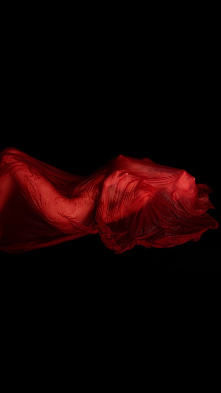 a photo of a woman draped in red fabric. the woman is laying down and the cloth covers her body. the photo is taken in a dark setting and the cloth is lit from behind, giving it a beautiful silhouette. the cloth seems to be made of a sheer fabric,  giving a sensual and suggestive feel.  the photo is artfully composed and is a beautiful example of abstract photography.