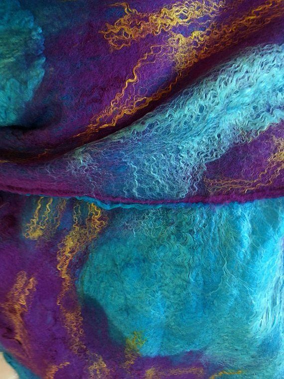 a closeup of a piece of felted wool fabric. the fabric is a mix of purple, blue, turquoise, and gold. the fabric is very soft and fluffy, and it has a beautiful texture. the fabric is handmade and it is a beautiful example of art.