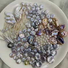 a closeup shot of a collection of beautiful pearls of varying sizes and shapes. they are arranged in a circular pattern on a white plate. the pearls have a soft, iridescent sheen and appear to be both white and silver. the image captures the beauty and elegance of these natural gems.