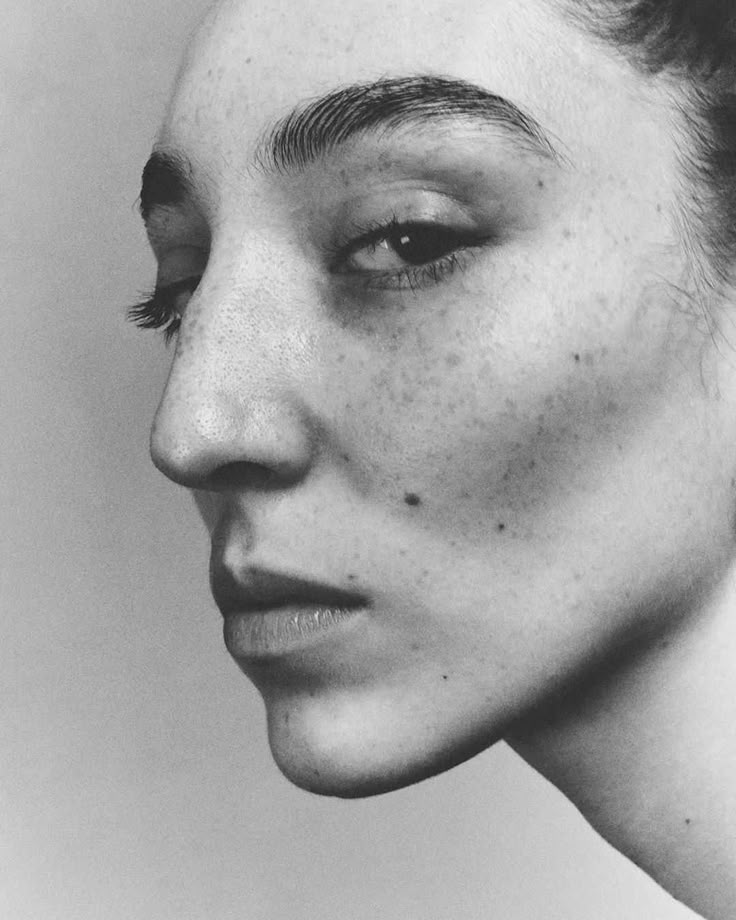 a closeup, black and white portrait of a woman's face in profile. the image highlights her freckles, distinctive eyebrows, and facial structure. she is looking slightly downwards.