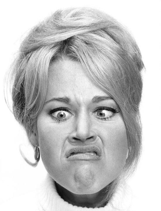 a black and white portrait of a woman, she has a pouty, serious expression on her face, with a slight frown and a narrowed gaze. she has short blonde hair that is styled back, with a few strands falling over her face. her eyes are large and dark, and her lips are slightly pursed together. she's wearing a lightcolored, collared sweater.