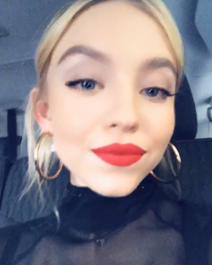 closeup shot of a young blonde woman wearing red lipstick and gold hoop earrings. she is looking directly at the camera, and her makeup is welldefined. she is sitting in what appears to be a car. the focus is sharply on her face.