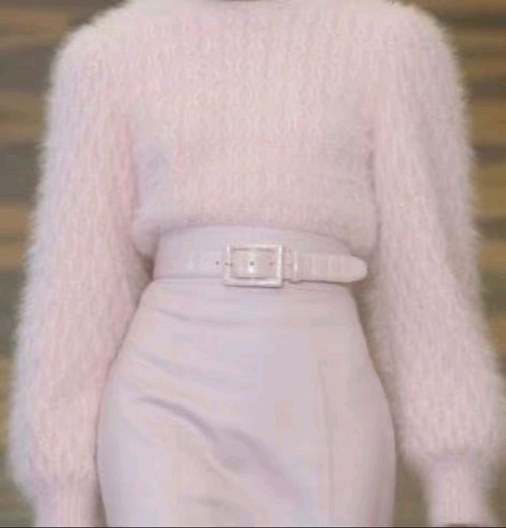 a woman wearing a soft, fluffy pink sweater and a white skirt with a white belt. the woman is standing in front of a light background. her outfit is elegant and stylish. she is wearing a fuzzy pink sweater with a white skirt and white belt.