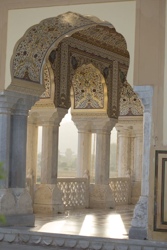 this is a picture of the interior of an elaborate building, most likely in india. there is beautiful detailed tiling work on the walls and ceilings. the arches are framed with intricately carved stonework.  this building is most likely of some historical significance.