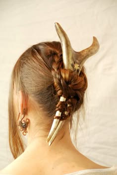 a young woman with long, braided hair is wearing an antler hair clip in her hair. the antler hair clip is a very unique and stylish accessory. she is also wearing a pair of earrings. she is looking away from the camera. the picture is welllit and the woman is looking at the camera.  she is very beautiful.