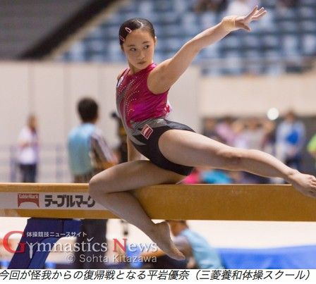 a young female gymnast performs a balance beam routine during a competition. she is wearing a pink and black leotard and has her arms extended above her head. the background is blurred and out of focus, with the focus on the gymnast.