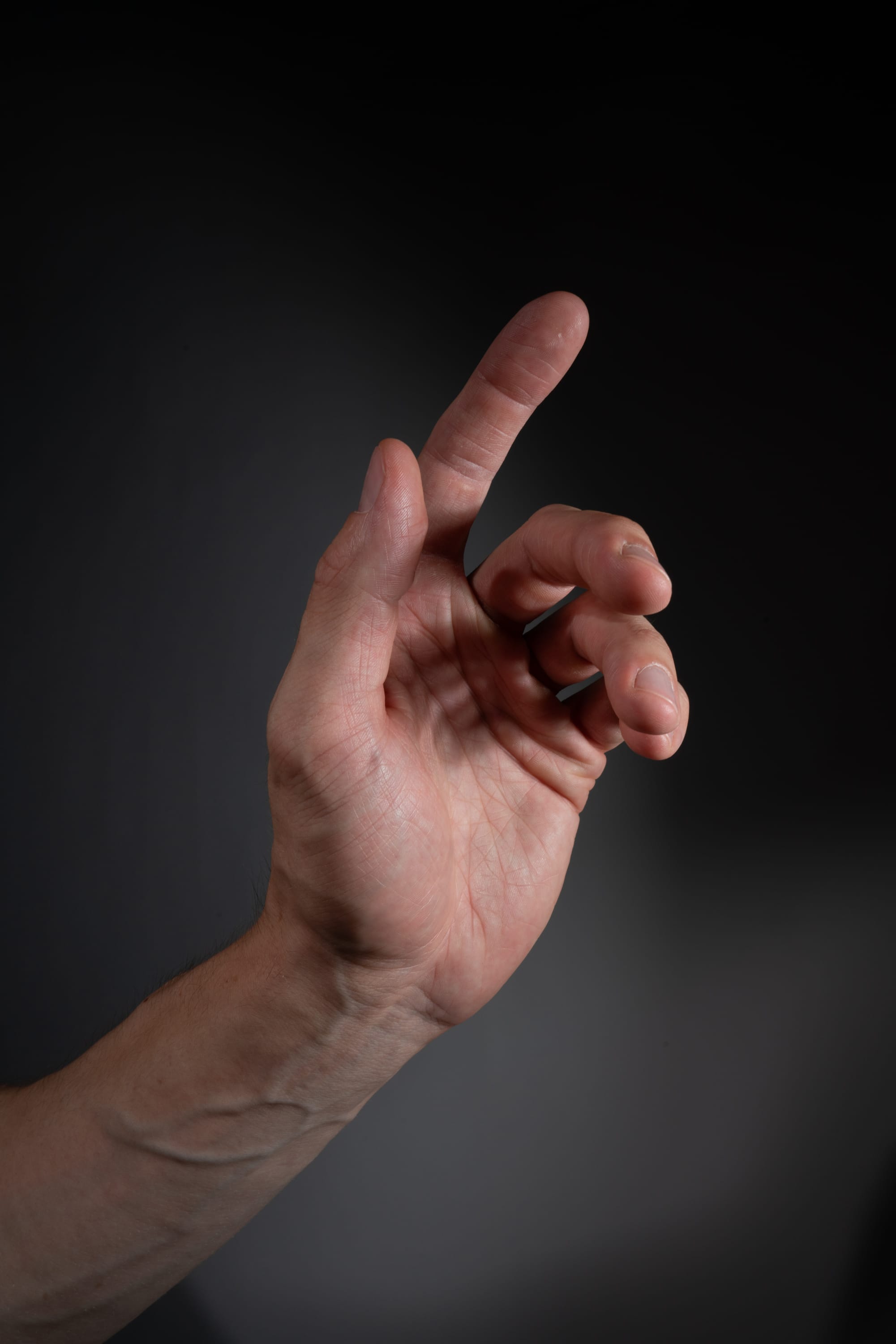 a man's left hand is extended with his index finger pointing upwards, set against a dark gray background.