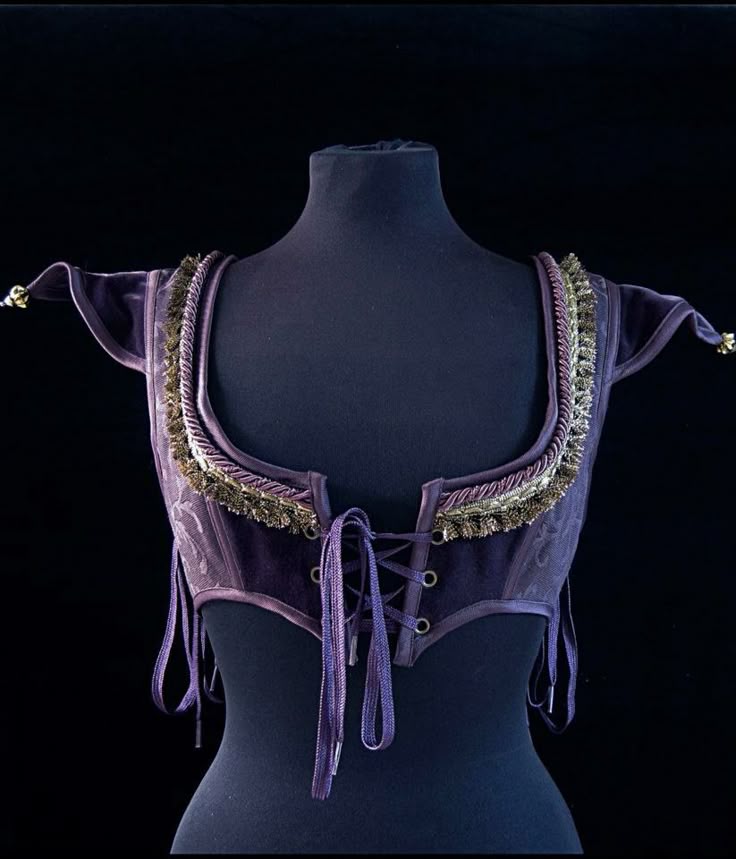 a purple velvet corset, with gold trim, is displayed on a black mannequin. the corset features a laceup front and a square neckline. it appears to be a vintage or renaissanceinspired costume piece.