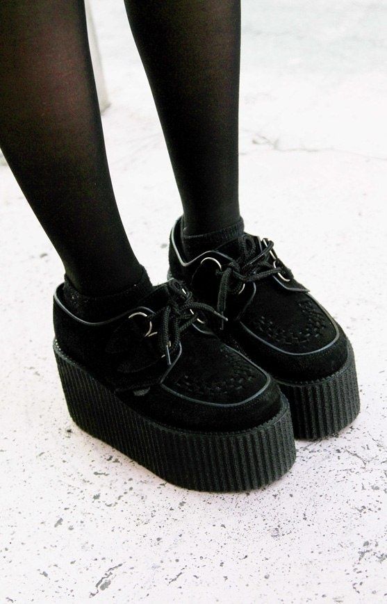 a closeup shot shows a pair of black platform creeper shoes worn with black tights. the shoes have a suedelike finish and a thick, ridged platform sole. the laces are tied, and the shoes appear to be in good condition. the background is a light gray surface.