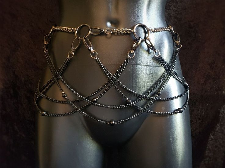 a closeup of a silver and black chain belt worn on a mannequin torso. the belt consists of a chain at the waist with cascading chains hanging down, some adorned with small beads.