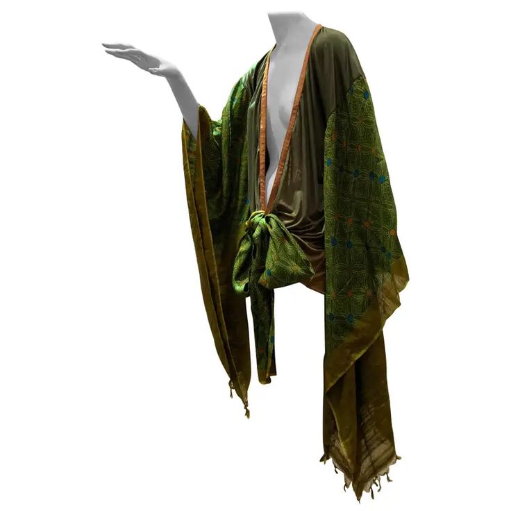 the image shows a vintage garment, possibly from the 1920s, displayed on a mannequin. the garment is a long, loosefitting robe or kimonostyle dress in shades of green and gold.  the fabric appears to be silk and features embroidered details. the robe is tied at the waist with a sash made from the same fabric.  the overall style suggests art deco influences or a flapper era design. the mannequin's arm is extended, showcasing the garment.  the background is plain white, isolating the garment for display.