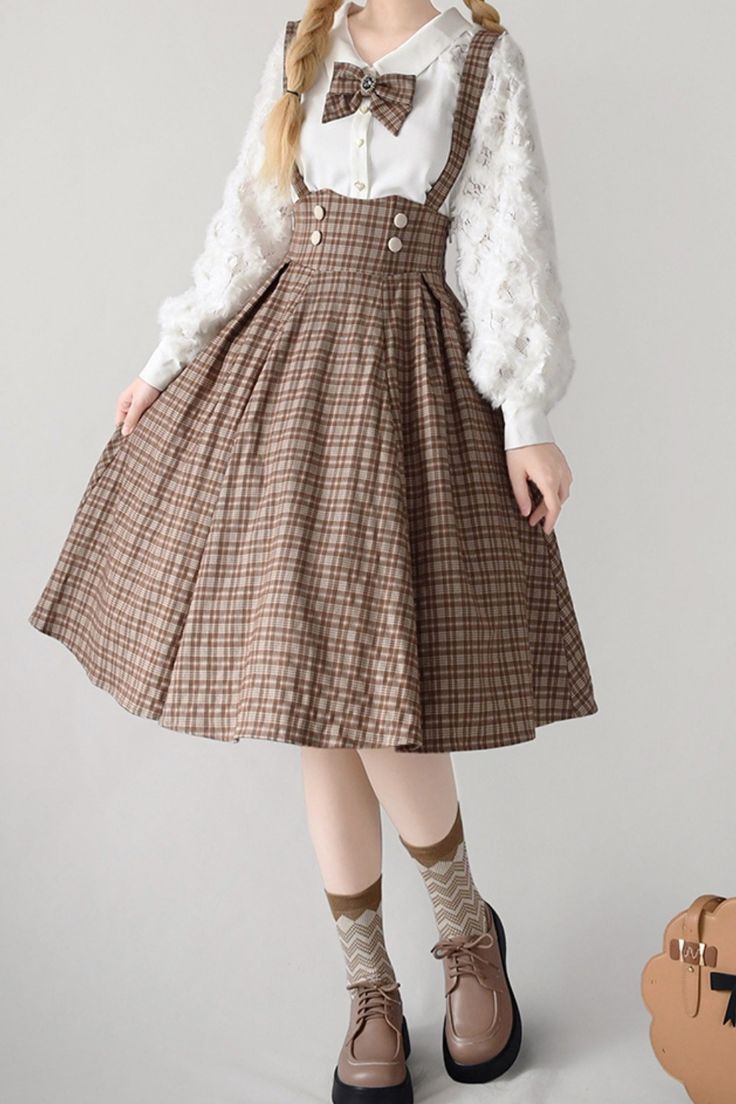 a young woman is modeling a brown plaid jumper dress with a white collared blouse. the dress features adjustable straps, a pleated skirt, and a doublebreasted button closure. she is also wearing brown oxford shoes and chevronpatterned socks. her hair is styled in braids, and she is wearing a brown bow tie. the background is a plain white wall.