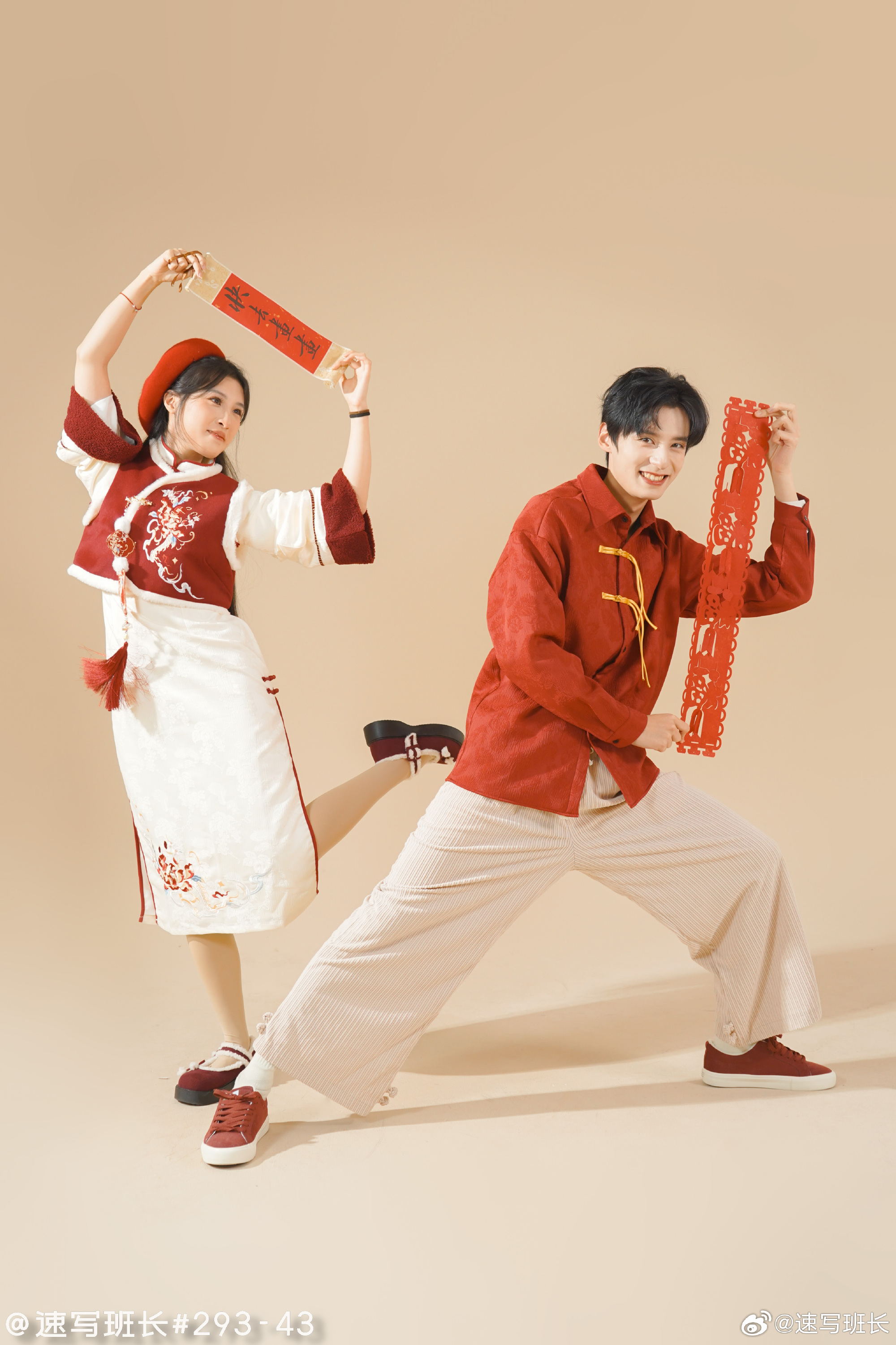 a young man and a young woman are striking playful poses for a chinese new year photoshoot. they're both dressed in festive red and white attire. the man wears a modernized version of a tang suit while the woman is in a more traditional qipaoinspired dress. they each hold red paper cutouts, likely representing good luck greetings for the new year. the image has a light and celebratory mood, emphasizing the joyous atmosphere of the holiday.