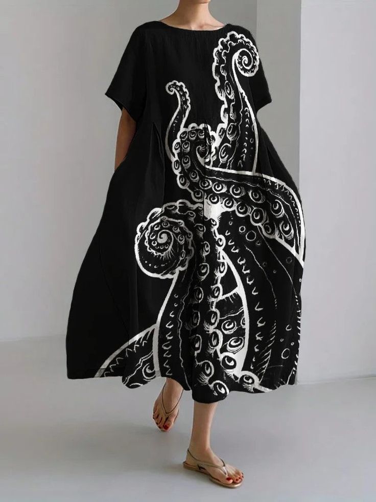 a woman in a black dress with a white octopus print stands in a studio setting. the dress is casual and summery, with short sleeves and a flowy skirt. the woman is wearing sandals, and her hair is pulled back from her face. the background is a simple white wall.