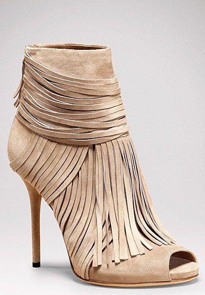 the image showcases a pair of elegant women's ankle boots.  they are made of light beige suede and feature a prominent fringe that extends from the upper shaft down to the peeptoe opening. the boots have a high, stiletto heel and a slender silhouette, suggesting a fashionable and possibly designer style. the background is a simple, lightgrey, which focuses attention on the boots themselves.