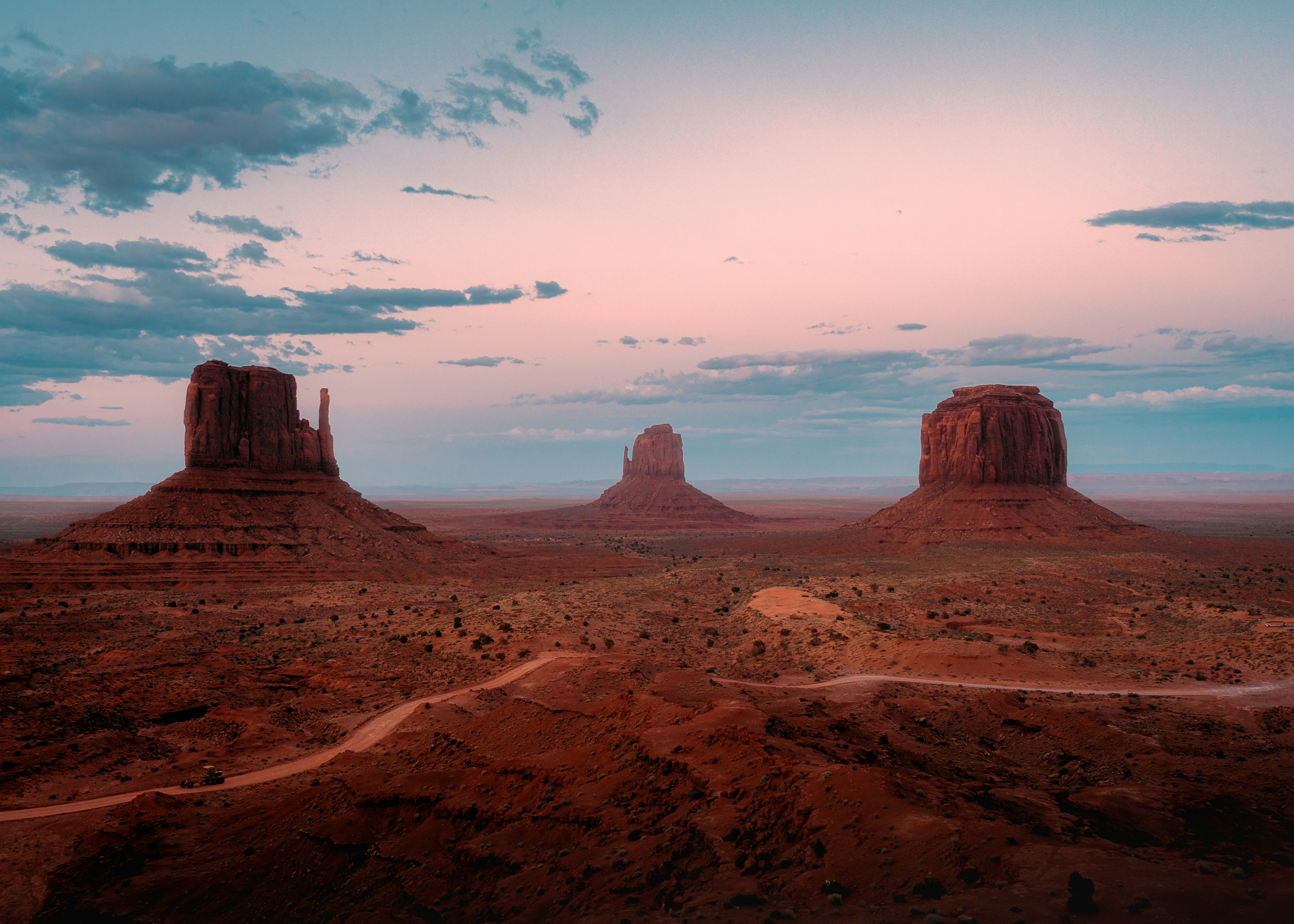 an aerial sunset view of monument valley, featuring its iconic sandstone buttes and mesas spread across the desert landscape. the warm hues of the setting sun cast a soft glow on the rock formations, creating a captivating and serene scene.