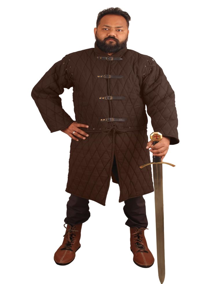 the image shows a man wearing a dark brown, long, quilted gambeson. the gambeson is a medievalstyle jacket with diamond quilting, fastened by leather straps and buckles.  he is also wearing brown leather boots and holding a longsword.  the setting appears to be a plain white background, suggesting a studio shot. the man's pose is relatively formal, and he's looking directly at the camera. the overall impression is of a man dressed in medievalstyle clothing for historical reenactment or a costume.