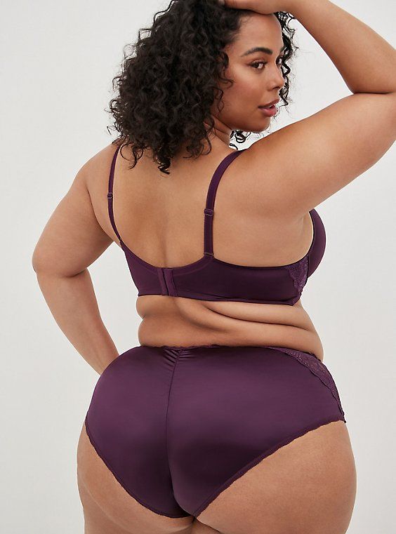 a rear view of a plussize, darkskinned woman modeling a set of dark purple lingerie. the image highlights her curves and promotes body positivity.