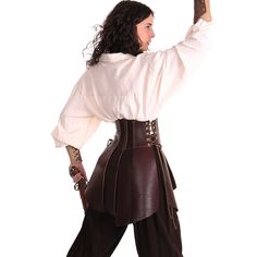 a woman is modeling a pirate costume in a studio setting. the costume features a brown leather corset over a white linen shirt. she is also wearing dark pants. the image is well lit and shows the details of the costume clearly.