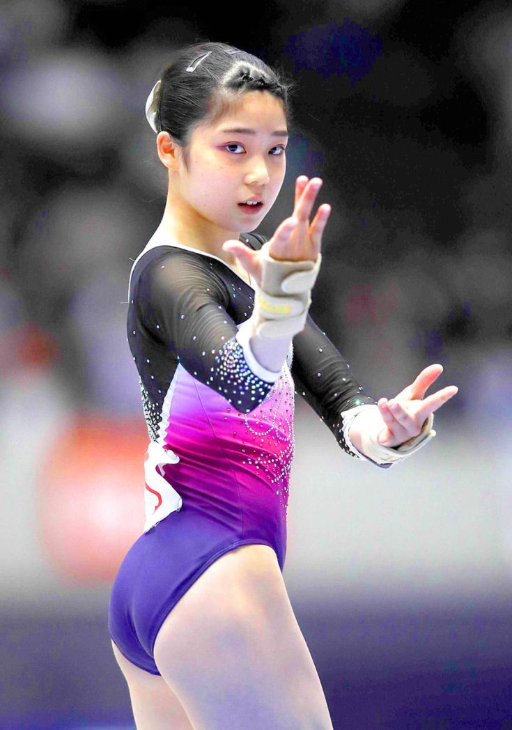 a young female gymnast in a purple leotard is posing during a floor exercise at a gymnastics competition. she is looking at the camera with a determined expression. the background is blurred.