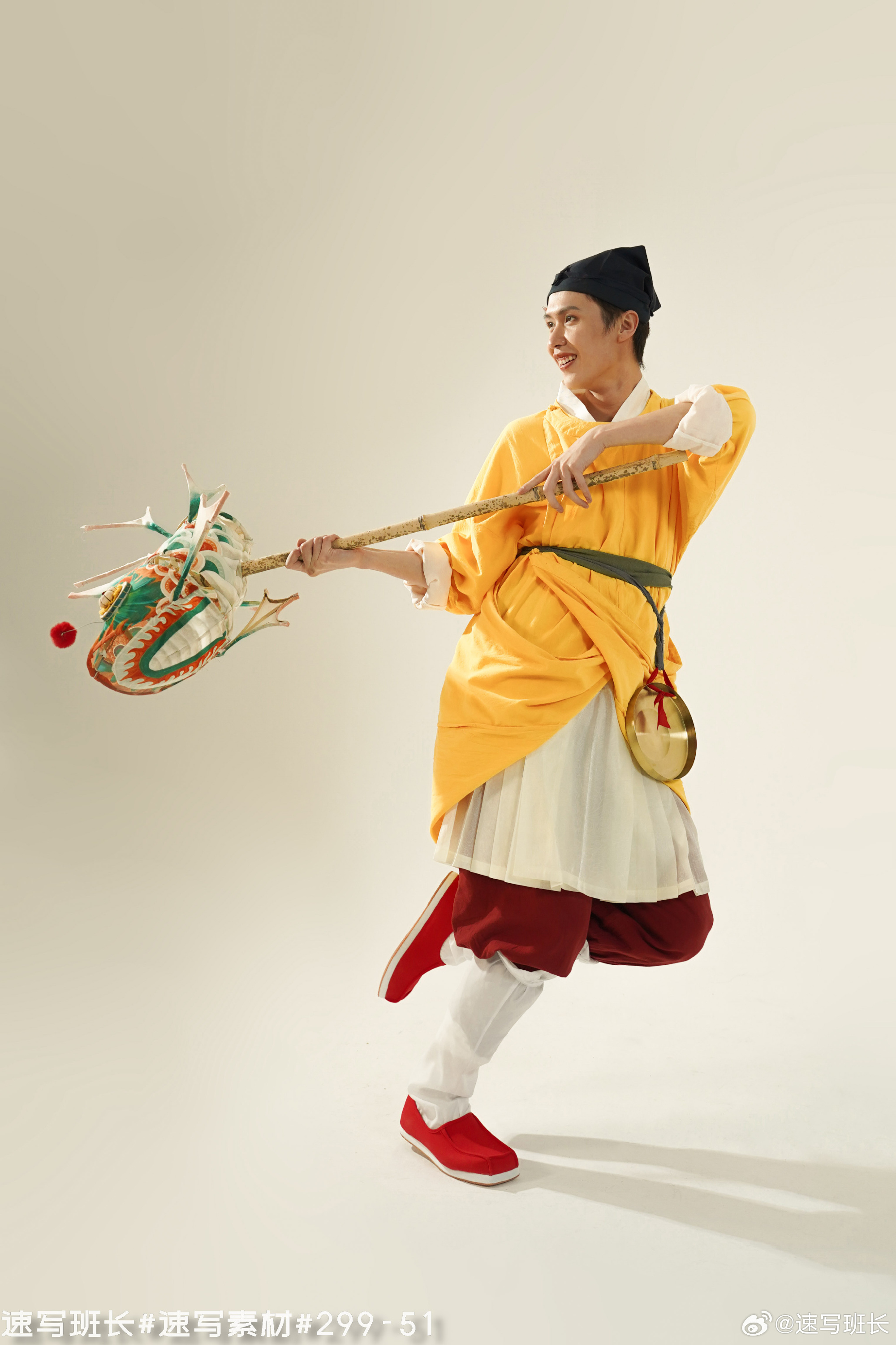a man dressed in traditional chinese clothing is performing a dragon dance. he is holding a long pole with a colorful dragon head attached to it, and he is smiling as he moves. the background is a plain white studio backdrop. the lighting is soft and artificial, and the perspective is from the front.