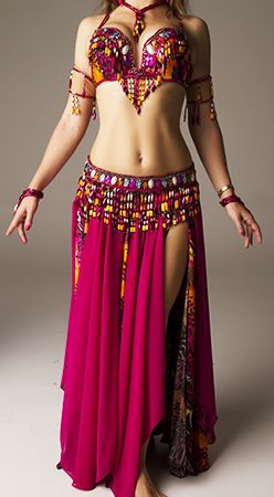 a woman in a colorful belly dancing costume is smiling and looking at the camera while holding her hands up in a traditional belly dance pose.