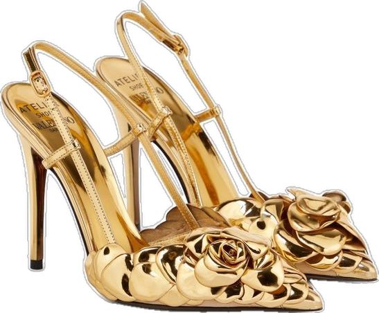 a closeup shot of a pair of gold valentino atelier high heels. the shoes are slingbacks with a stiletto heel and feature a large, sculpted rose detail on the toes. the shoes are metallic gold and appear to be made of a smooth, possibly leatherlike material.  the valentino branding is visible on the insole. the image is set against a plain white background.