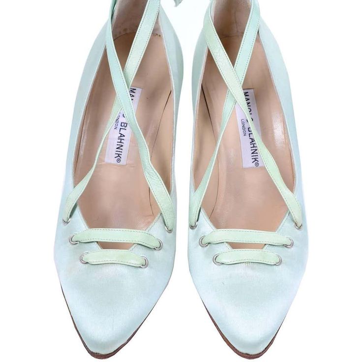 a pair of manolo blahnik light green satin heels with crisscross ankle ties and pointed toes.  the shoes are preowned and show the brand label inside. the color is a pale, delicate mint green. the satin fabric gives the shoes a luxurious feel. the image shows both shoes from an overhead perspective, highlighting the design details and condition.
