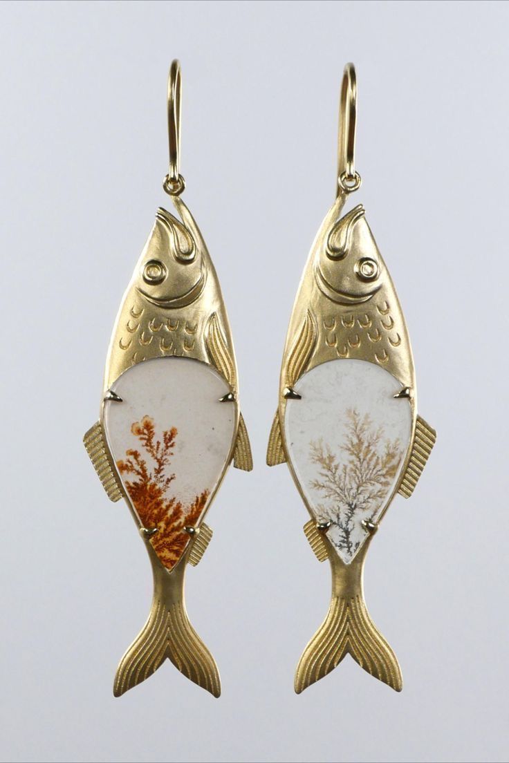 a pair of fishshaped dangle earrings with gold bodies and white agate stone insets, each featuring a dendrite pattern. the earrings have gold hooks for pierced ears.