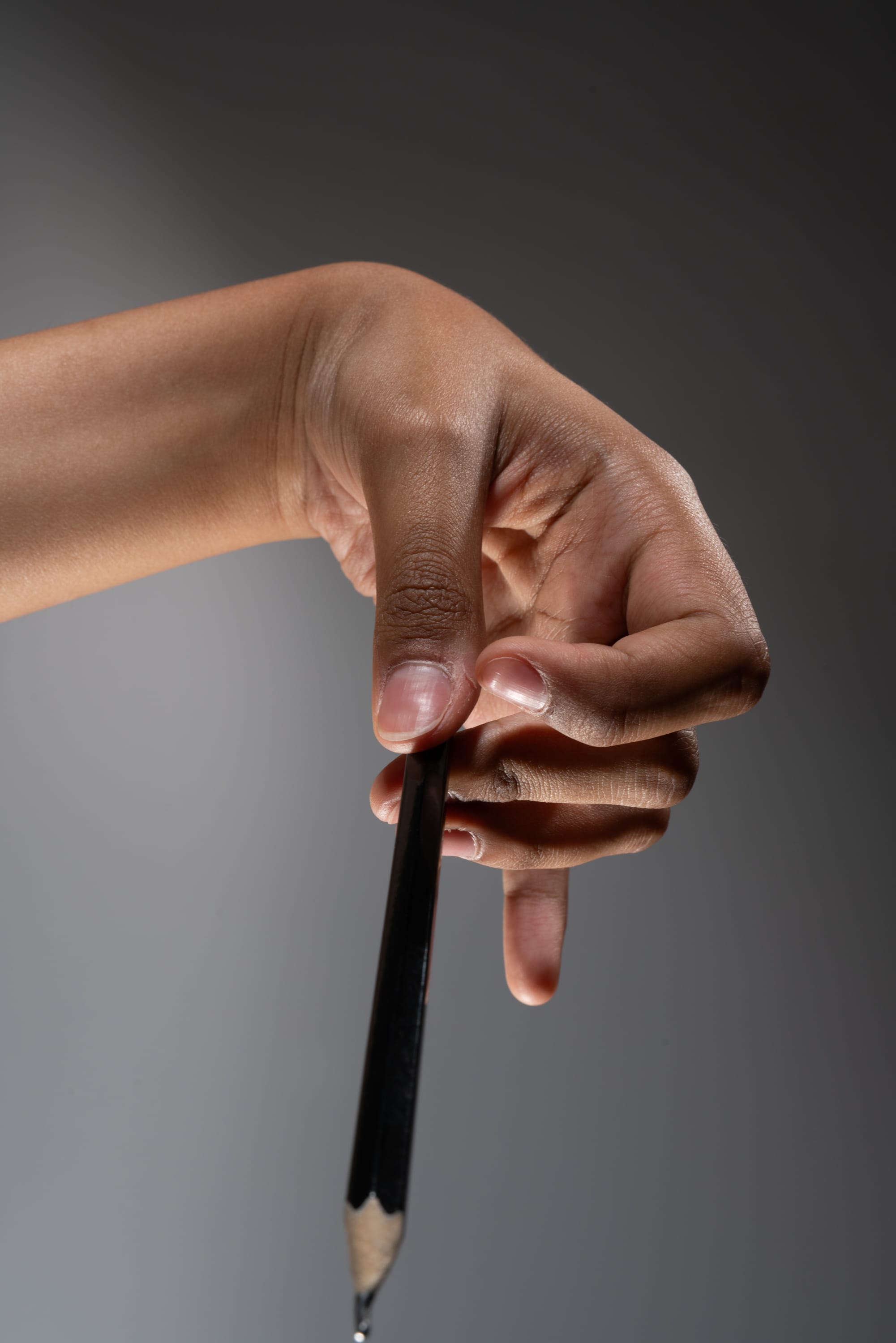 the image is of a hand holding a black pencil against a gray background. the hand is holding the pencil as if it is about to write or draw something. the lighting is soft and highlights the texture of the hand and the pencil.