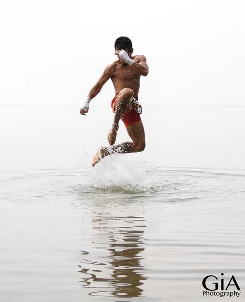 a man in red shorts jumps into the water after doing a martial arts move, with a white background and water splash coming up behind him.
