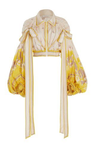 this image shows a women's cropped jacket in a yellow and cream floral print. the jacket has long puff sleeves and is decorated with long ribbons tied into bows at the shoulders.  the jacket appears to be made from a luxurious silk or satin material.  the overall style is highfashion and feminine.